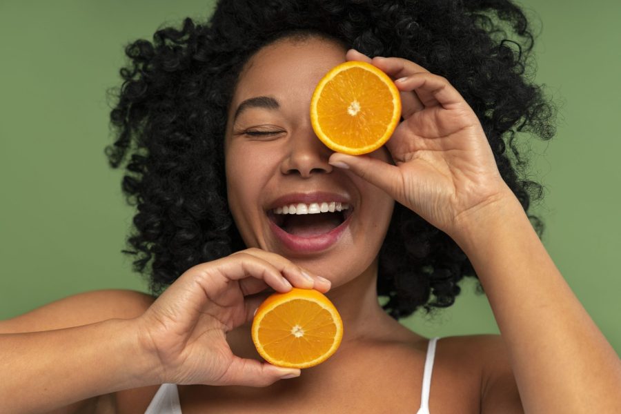 Mulher negra rindo e segurando duas laranjas para remeter os benefícios da vitamina C