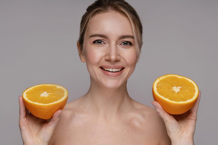 Mulher segurando duas laranjas para representar a vitamina c e os benefícios encontrados em produtos de cosméticos